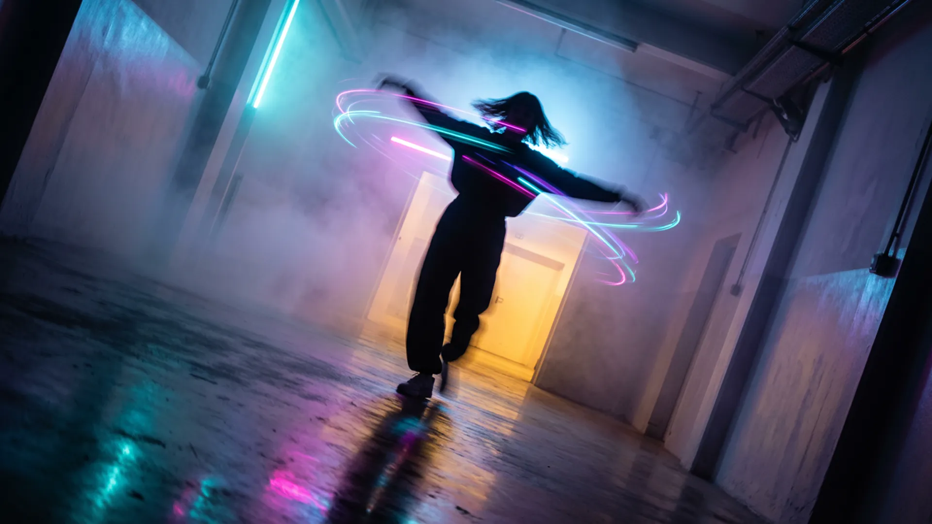 In a burst of uninhibited movement, a figure is captured mid-spin in a corridor of light and mist. The photography freezes the action at its peak, the personโs arms flung wide, their head tilted back in a moment of pure, kinetic release. This rapid twirl has visibly disturbed the dense, colored fog, creating eddies and vortices of cyan, magenta, and violet light around their silhouetted form. The composition is vibrant and chaotic, a stark contrast to a static scene. Light from a warm, yellow-orange portal ahead illuminates the swirling mist from one direction, while a cool blue glow from behind adds depth and complexity to the color palette. The floor, a dark mirror, reflects a blurred, chaotic version of the sceneโa painterly smear of motion and color. The camera angle is slightly tilted, a Dutch angle that enhances the feeling of disequilibrium and exhilaration, capturing a fleeting, joyful rebellion against the quiet, contemplative nature of the space